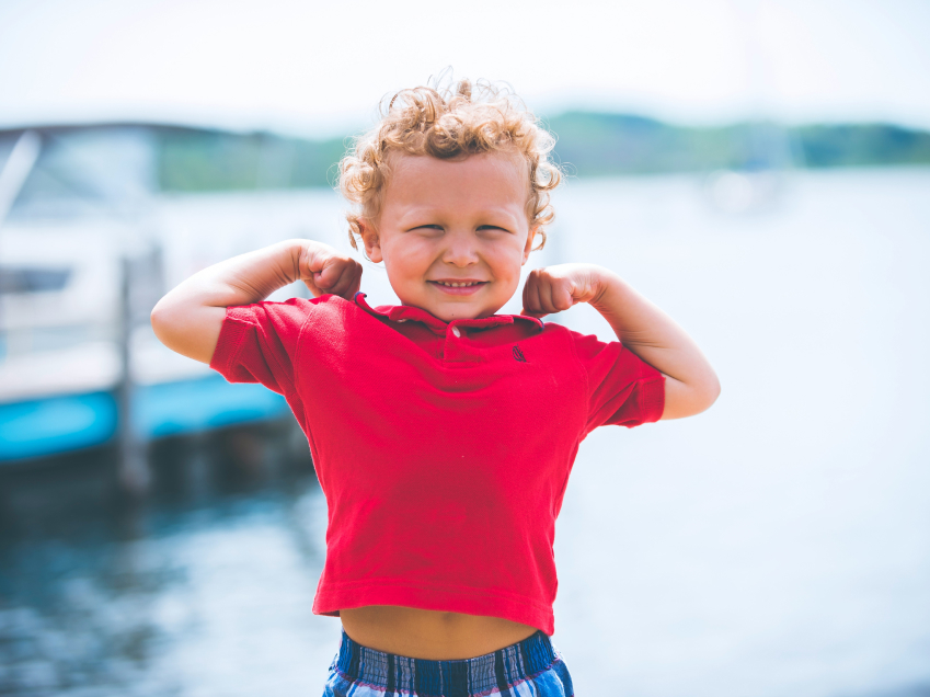 Child flexing arms in front of a lake